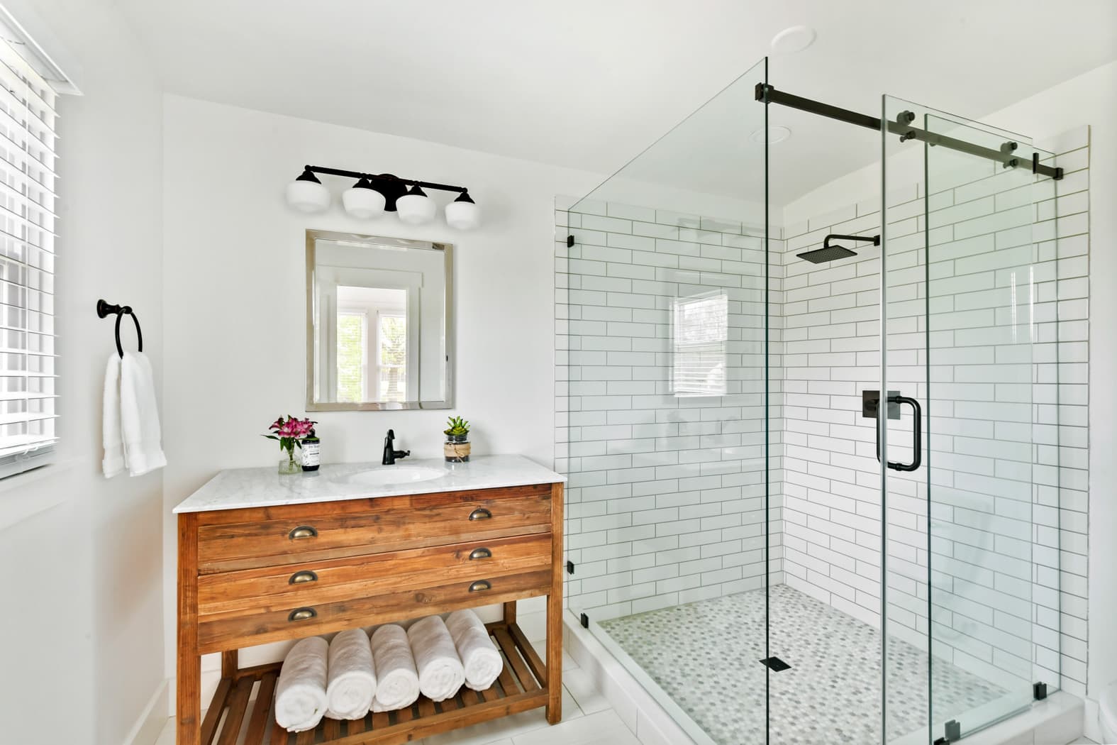 A modern bathroom featuring a rustic wood vanity with a white marble top, a large walk-in shower with glass doors and white subway tile, and black hardware accents.