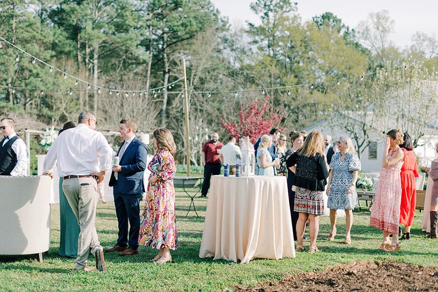 A lively outdoor gathering with guests mingling around tables in a garden setting.