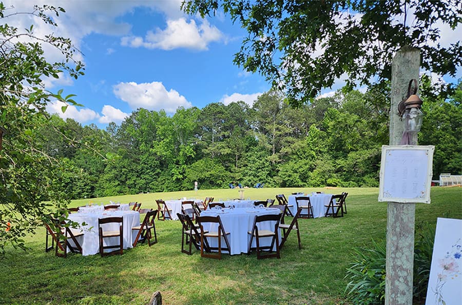 Outdoor event setup with round tables and chairs surrounded by greenery.